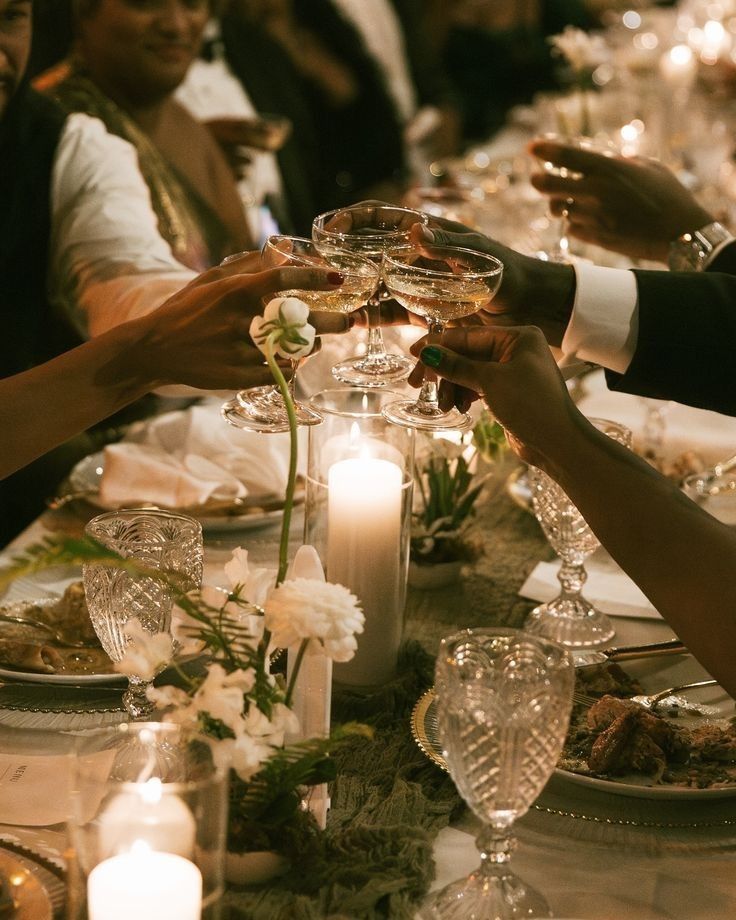 Guests raising coupes of champagne over a candlelit dinner table.