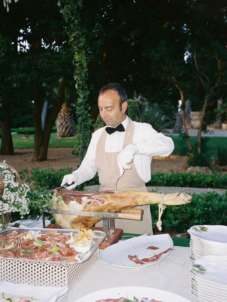 A server in a bow tie carving a ham at a station in the garden.