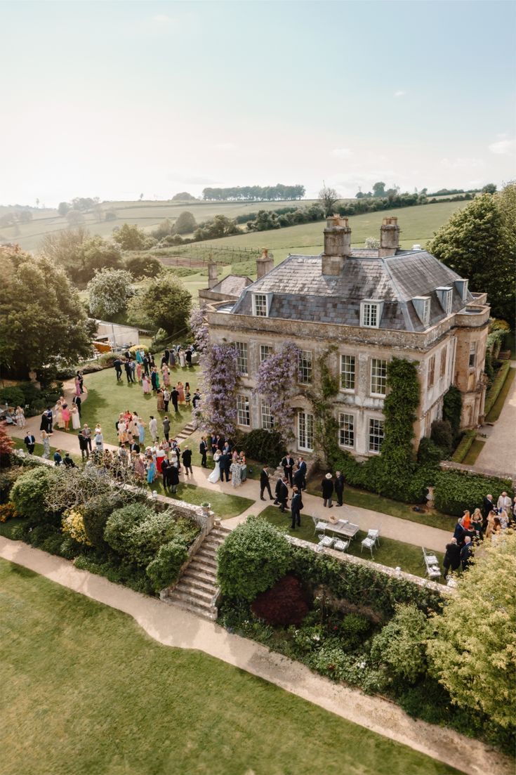 The manor from above: a pale stone Georgian house with wisteria on its walls, and guests gathered on the lawns and terraces around it.