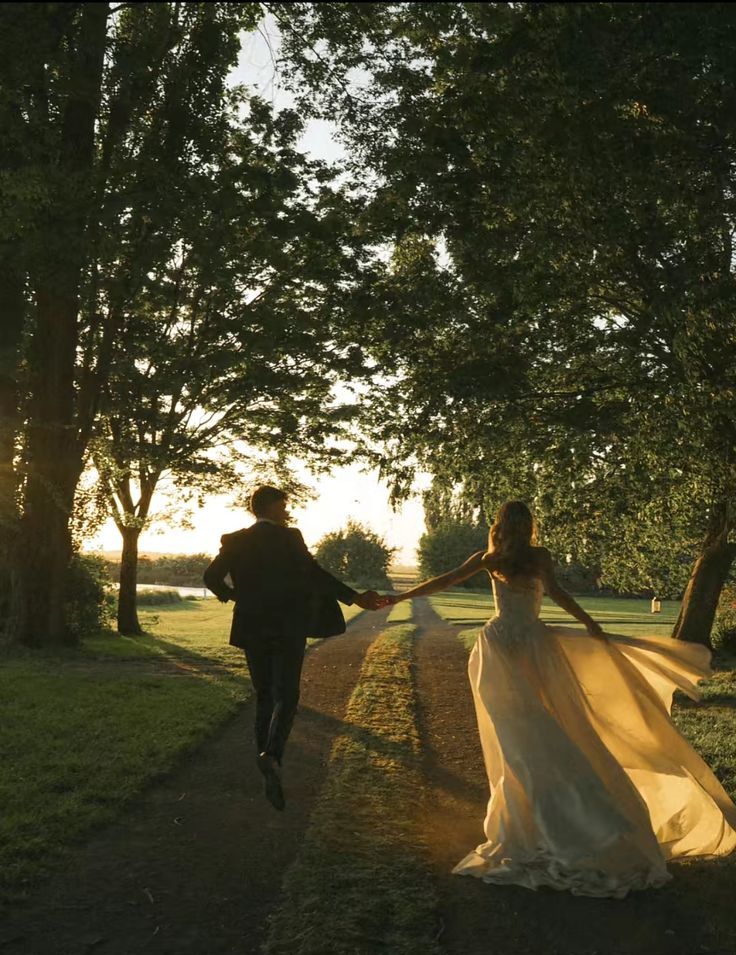 A couple running hand in hand down a tree-lined path at golden hour.